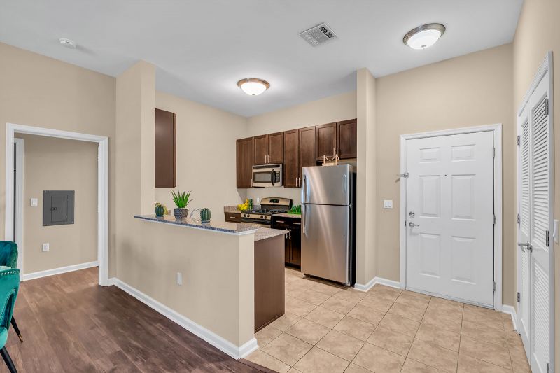Interior photo of a model at Helix at Xchange showcasing the kitchen with luxurious slate tile flooring. The kitchen features new wood cabinetry, granite countertops, and stainless-steel appliances. To the right, the front entrance is visible along with an additional opening that leads to other areas of the unit.