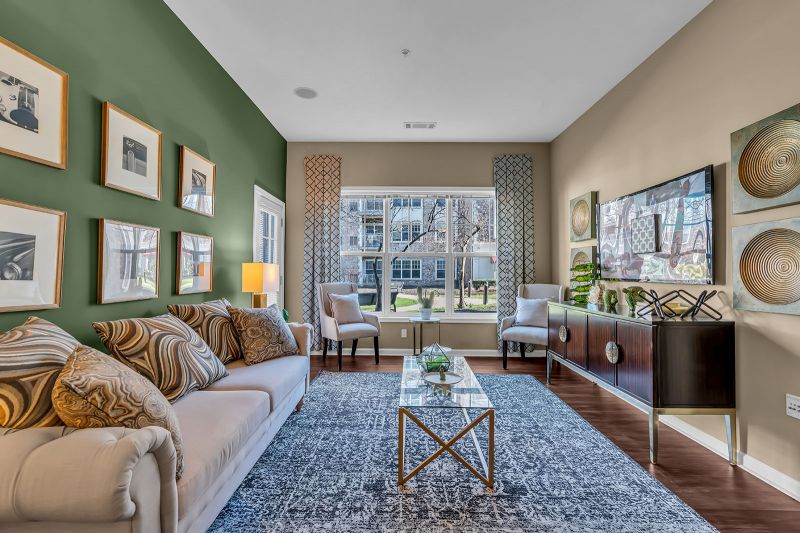Interior photo of a model at Helix at Xchange showcasing the living room featuring luxury hardwood flooring. The space features a large couch, two accent chairs, a coffee table, and a stylish console for added storage. Elegant decor and artwork enhance the room, while a large window fills the space with natural light.