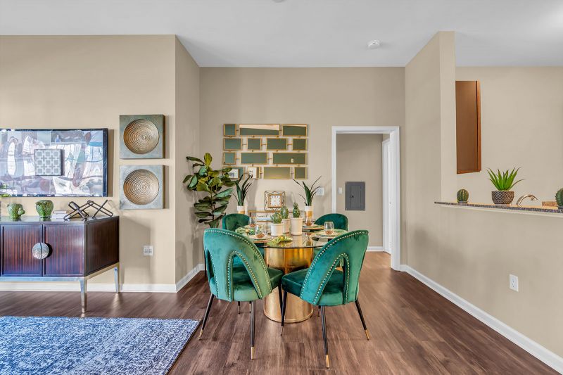 Interior photo of a model at Helix at showcasing the dinette area with luxurious hardwood flooring. The space includes a circular table surrounded by four stylish chairs. In the background, an open doorway offers a view into additional areas of the unit.