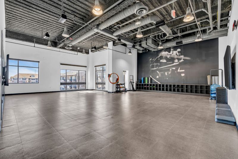 Interior photo of the movement studio at Xchange at Secaucus showcasing a spacious, open layout with padded flooring—ideal for yoga flows, Pilates, barre workouts and stretching routines. The studio is equipped with medicine balls, dumbbells, and stability balls to support a variety of workouts, along with a large wall-mounted TVs for streaming fitness classes or guided sessions.