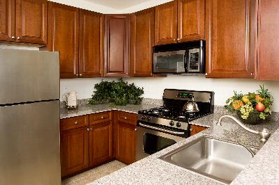 Towne Centre at Englewood kitchen photo showing cherry cabinets, stainless steel appliances, granite countertops and ceramic tile flooring. Several plants, a tea pot and other decorations are displayed on the counter.