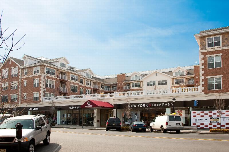 Towne Centre at Englewood front exterior photo showing the street level retail and the apartments above. Several cars are parked in the retail section. The apartments above are a combination of brick and stone with white trim.