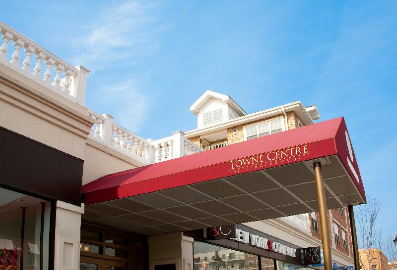 Towne Centre at Englewood front exterior photo showing the awning over the main entrance. The awning is a deep red color and features the property name, Towne Centre at Englewood in gold lettering.
