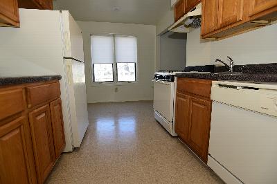 Peach Street Kitchen photo showing maple color cabinets, tile flooring and white appliances. Two windows allow natural light to enter the room.
