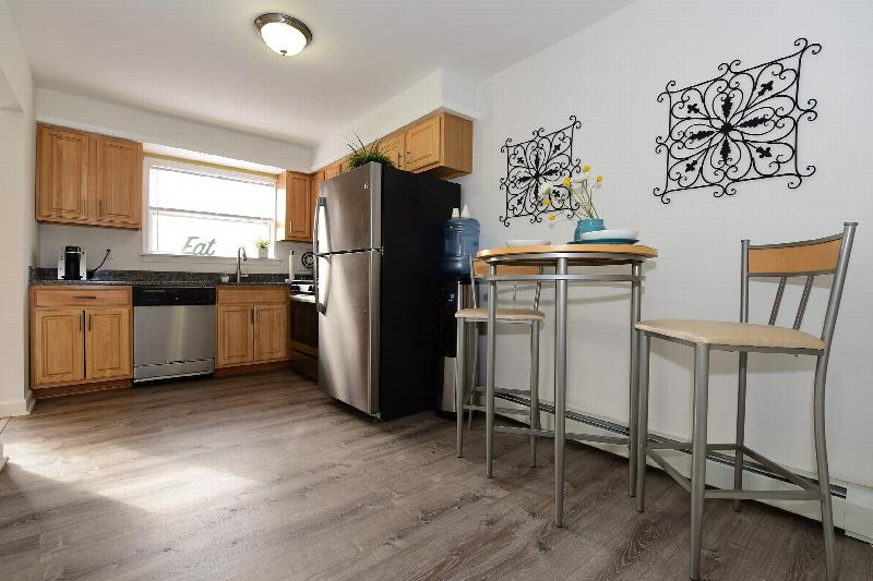Delaware Heights kitchen showing maple color cabinets. granite countertops, stainless steel appliances, wood grain flooring and a bistro table with seating for two.