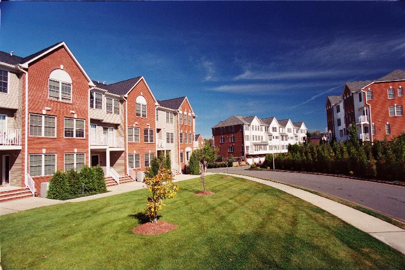 Exterior photo of Sun Valley Plaza showing several three story apartment buildings and a large grass area. Many bushes and trees landscape the area.