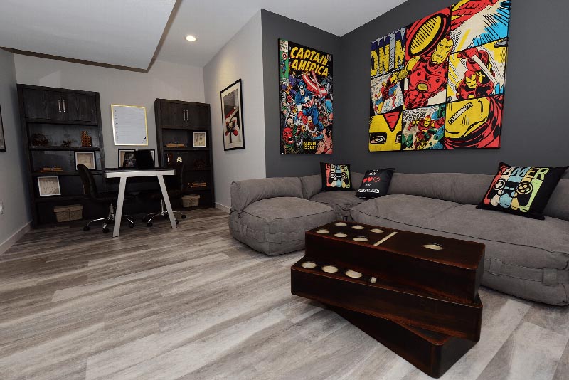 Sun Valley Plaza photo of a rec room with a sectional couch, a desk and multiple book shelves. The room features wood grain tile flooring.