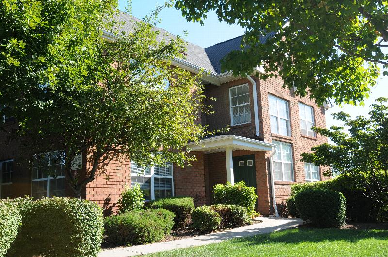 New Center Greens Exterior photo showing the entrance to an apartment. Several bushes and trees highlight the landscape.