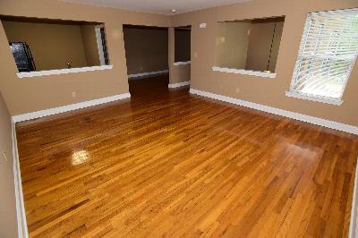 New Center Greens Living Room photo displaying hardwood floors that run the length of the apartment. The kitchen and hallways can be seen in the background.