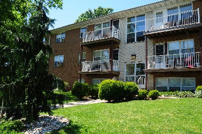 Exterior photo of Wilder Manor showing a two story apartment building. There is a staircase leading to the main entry, and balconies on both the first and second floors. Trees, shrubs and green grass landscape the area.