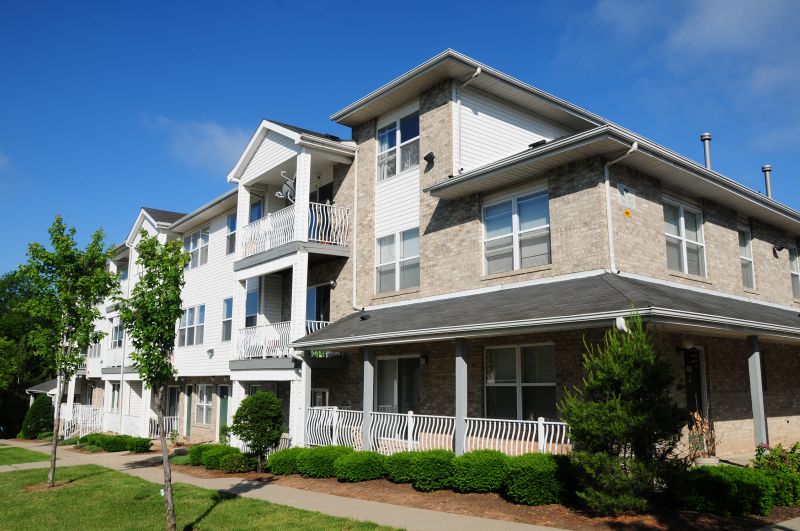 Tyler Greens apartments photo of the exterior shows a three level brick and siding apartment building with balconies and green entry doors and white trim.