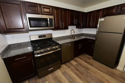 Photo of renovated kitchen at Tyler Greens showing wood grain flooring, new cherry cabinets, granite countertops, ceramic tile backsplash and new appliances.
