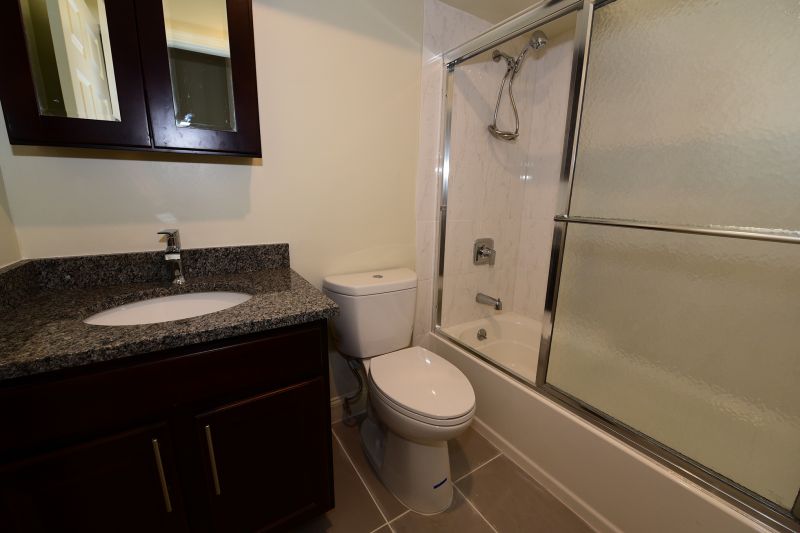 Photo of renovated bathroom at Tyler Greens showing new tile floor, vanity with granite countertop, medicine cabinet with mirror, new tub with shower door, and a new toilet.