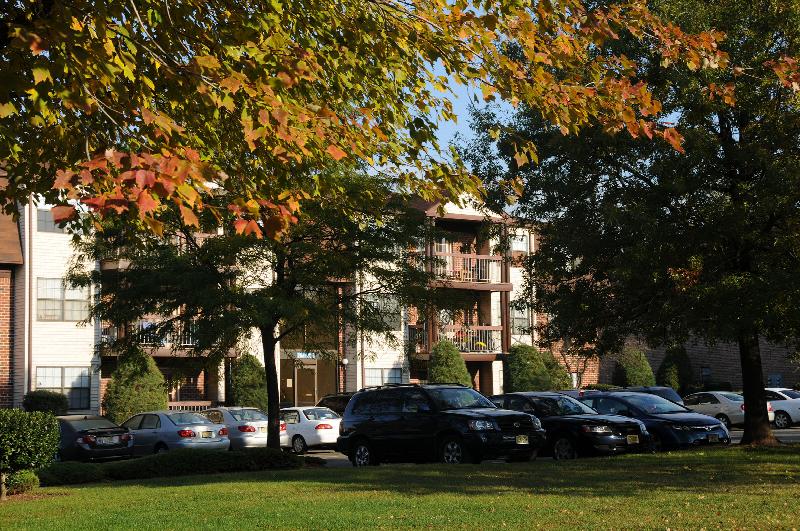 Green Plaza exterior photo shows a story apartment building with brick, cream siding and balconies on all three floors. A large parking lot in front of the building showcases the ample parking.