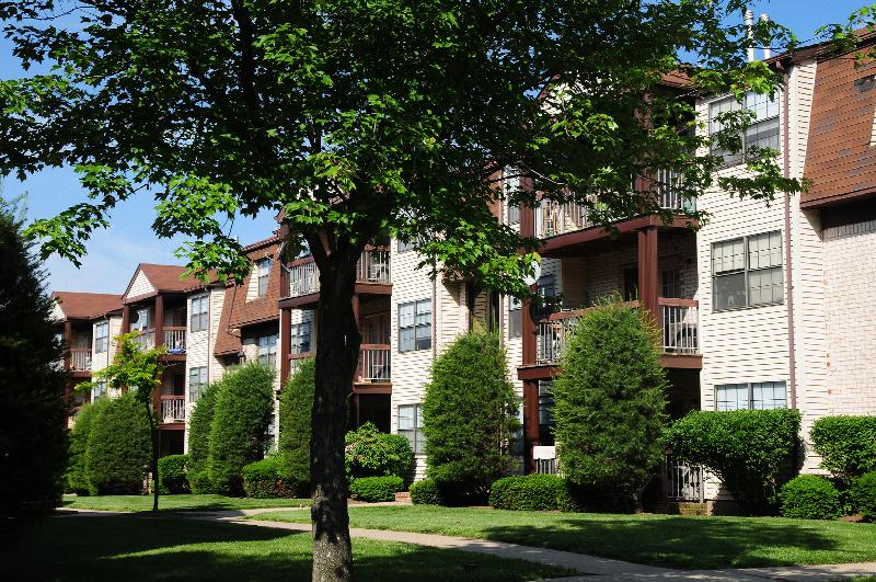 Green Plaza exterior photo shows a story apartment building with brick, cream siding and balconies on all three floors. Green grass, bushes and trees landscape the area.