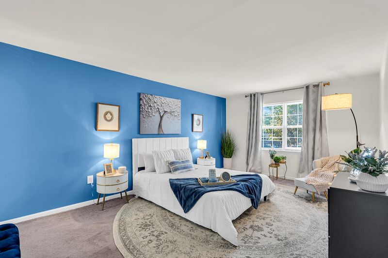 Interior photo of the bedroom at Green Plaza showing a twin-size bed, two nightstands, and a dresser with wall-to-wall carpeting. Large window to allow for natural light.