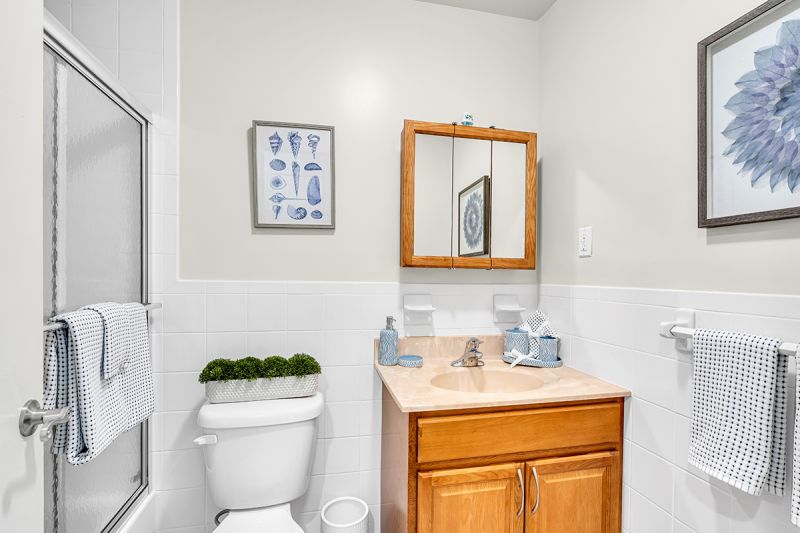 Interior photo of the bathroom at Green Plaza showing a sink with granite tops, medicine cabinet with attached mirror, a toilet, and shower with glass sliding doors.