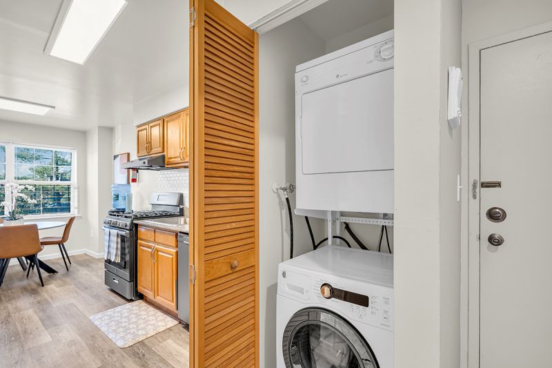 Interior photo of the laundry space at Green Plaza showing a full-size washer and dryer with pull-out sliding doors. The eat-in-kitchen can be seen in the background.