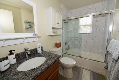 Photo of a refurbished bathroom at Florida Grove Manor showing new tile floor, new tub with glass doors, new vanity with granite countertop, medicine cabinet and mirror above