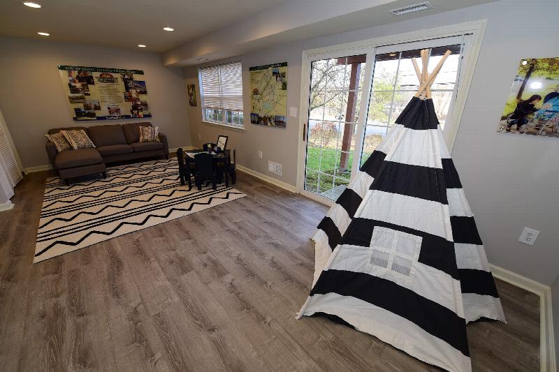 Yorkshire Meadows finished rec room showing a seating area for adults and children as well as a few toys. There is a sliding glass door leading to the outside.