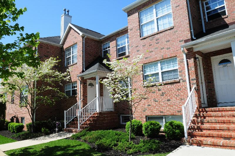 Homestead Village exterior photo of a full brick apartment building showing multiple staircases leading to front doors. Green grass, shrubs and flowering trees landscape the front of the building.