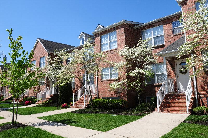 Homestead Village exterior photo of a full brick apartment building showing multiple staircases leading to front doors. Green grass, shrubs and flowering trees landscape the front of the building. Sidewalks and entrance walks are also shown.