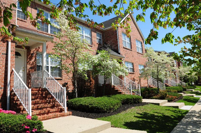 Homestead Village exterior photo of a full brick apartment building showing multiple staircases leading to front doors. Green grass, shrubs and flowering trees landscape the front of the building.