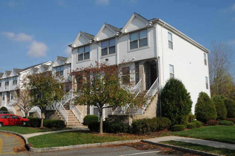 Evergreen Forest exterior photo shows townhomes with brick and white siding. Stairs lead to front door entries. Grass and green bushes landscape the area around the building.
