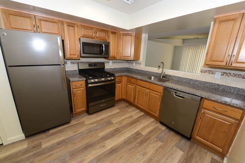 Photo of a renovated kitchen at Evergreen Forest showing vinyl wood plank flooring, granite countertops, new appliances, new cabinets and mosaic tile backsplash.