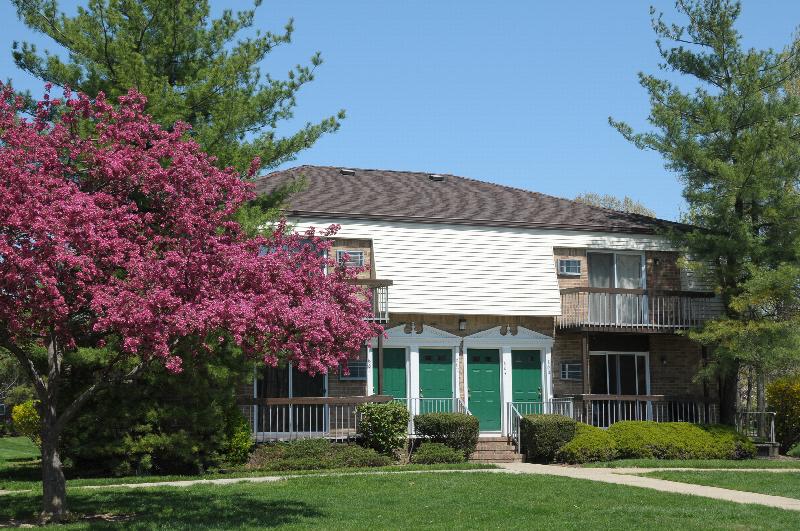 North Brunswick Manor Exterior photo showing a brick exterior and several balconies. Several bushes and trees highlight the landscape.