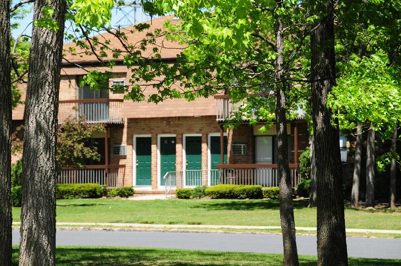 North Brunswick Manor Exterior photo showing a brick exterior and several balconies. Several bushes and trees highlight the landscape.