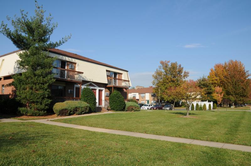 North Brunswick Manor Exterior photo showing a brick exterior and several balconies. Several bushes and trees highlight the landscape.