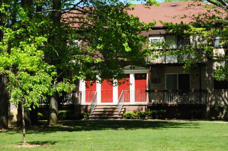 North Brunswick Manor Exterior photo showing a brick exterior and several balconies. Several bushes and trees highlight the landscape.