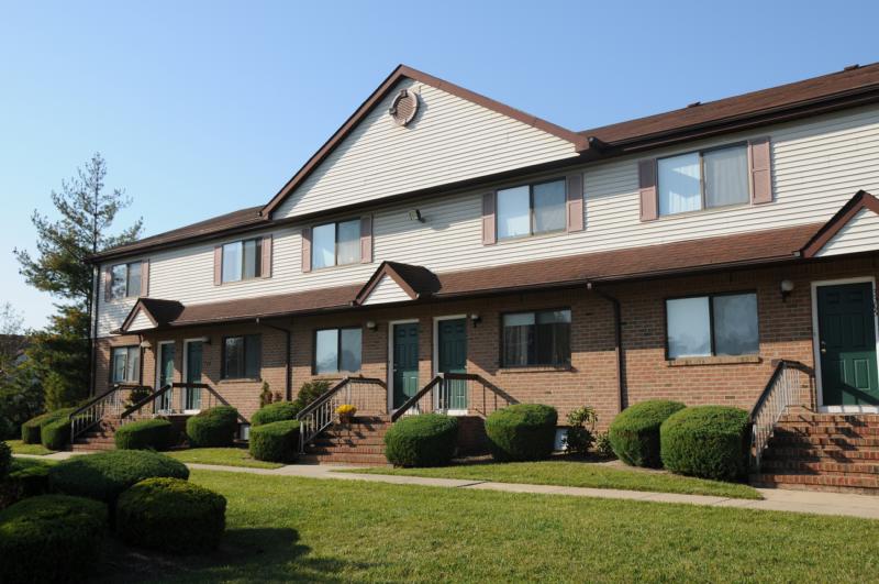 North Brunswick Manor Exterior photo showing a brick exterior and several apartment entrances. Several bushes highlight the landscape.