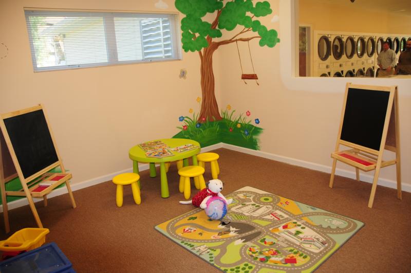 North Brunswick Manor Children’s Playroom photo showing a small table with chairs and several games. There are two chalkboards and toys around the room. The laundry room can be seen from the playroom.