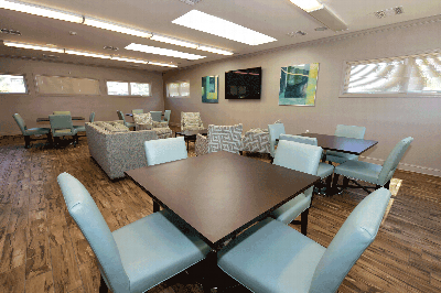 Photo of North Brunswick Manor Clubhouse Community room showing wood grain flooring, multiple seating areas and a large screen TV mounted on the wall.