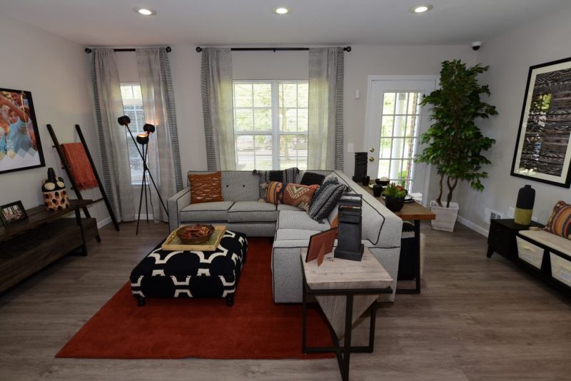 Maebrook at Renaissance interior photo of a living room showing a large sectional couch with ottoman, wall mounted TV, recessed lighting, several windows and a door leading to the outside.