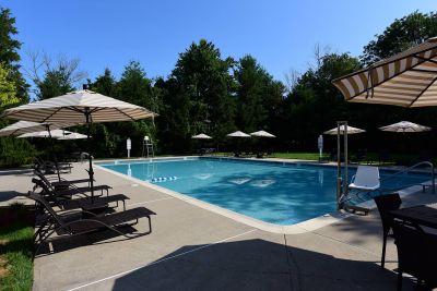 Maebrook at Renaissance Swimming Pool photo showing several small tables with umbrellas and several lounge chairs. Several bushes and trees highlight the landscape around the pool.
