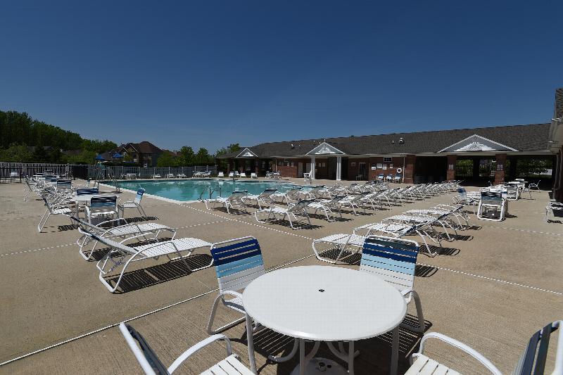 Woodhaven Terrace Pool photo showing a large pool next to the Swim Club with several reclining chairs. The apartment complex can be seen in the background. Several bushes and trees highlight the landscape.