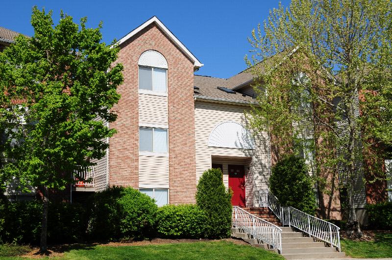Harbortown Terrace exterior photo of a 3 story apartment building. There is a sidewalk leading to stairs that bring you to the front entrance. Trees, bushes and green grass landscape the area.