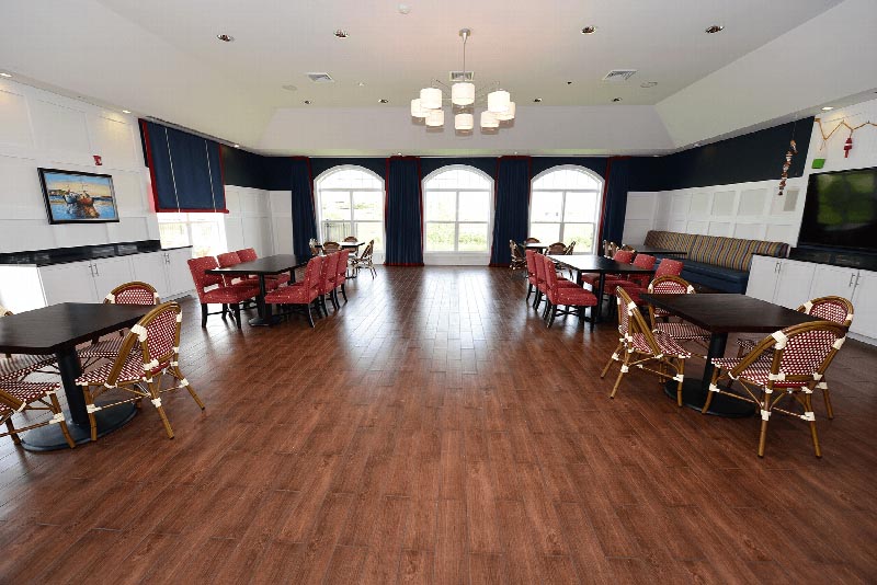 Harbortown Clubhouse community room photo showing multiple seating areas and a large screen TV mounted on the wall. There is hardwood floors and a large window to allow for natural light.