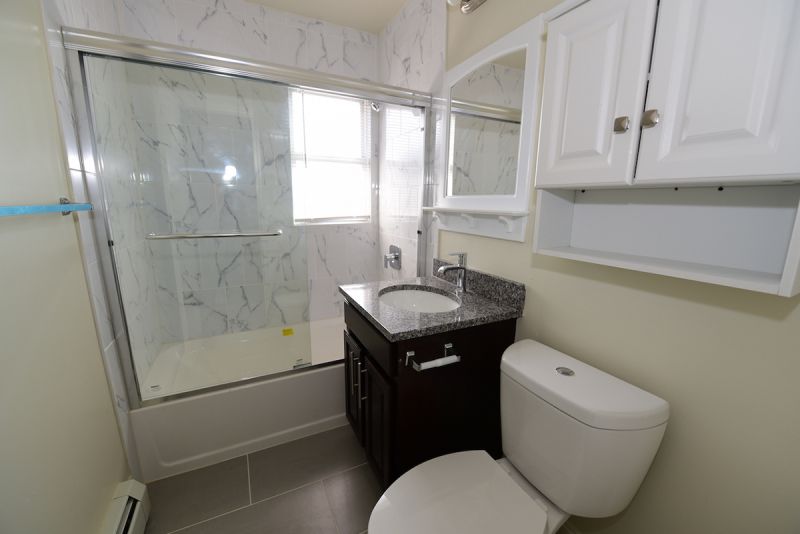 Photo of a refurbished bathroom at Convery gardens showing new tile floor, new tub with glass doors, new vanity with granite countertop, medicine cabinet and mirror above
