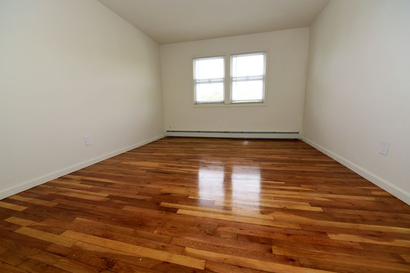 Photo of a refurbished bedroom at Convery Gardens, showing refinished hardwood floors and new paint.  Large window allows for natural light
