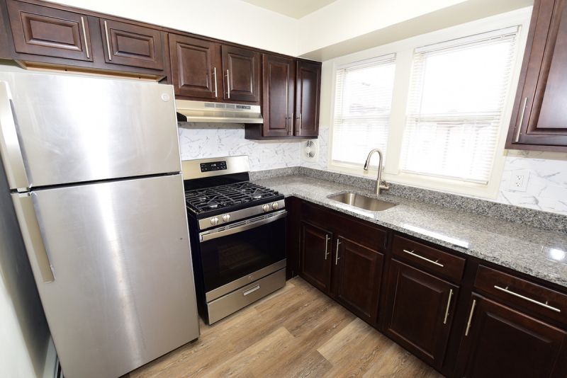 Photo of a refurbished kitchen at Convery Gardens showing new cherry cabinets, stainless steel appliances, granite countertops and luxury LVT woodgrain flooring.