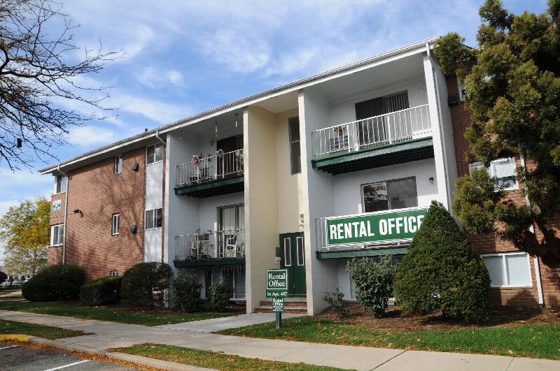 State Fayette Exterior photo showing a brick exterior and several balconies. There are two signs for the Rental Office. Several bushes and trees highlight the landscape.