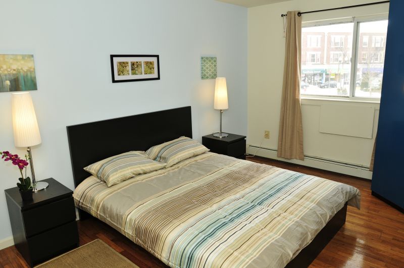State Fayette Bedroom photo showing a queen sized bed and two night stands with lamps. There are several decroations on the wall and on the night stands. There is a window to allow natural light to enter the room.