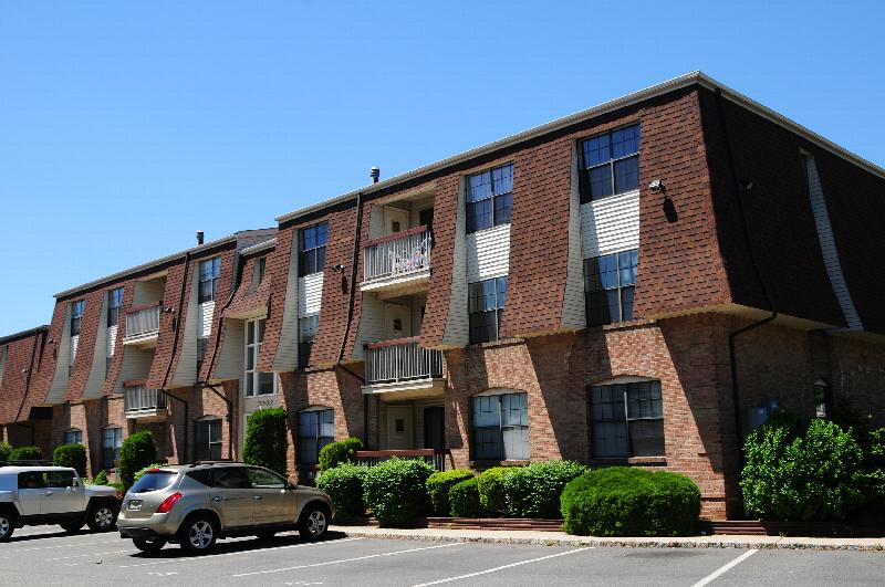 Hidden Village exterior photo showing a 3 story apartment building with balconies. A large parking lot supplies ample parking for tenants.