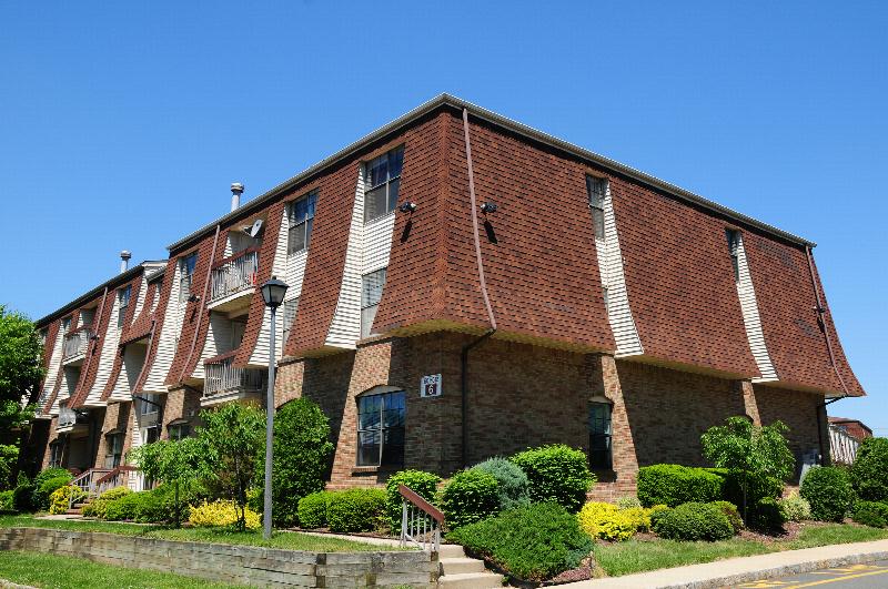 Hidden Village photo of an apartment building showing many green bushes ad green grass landscaping the area.