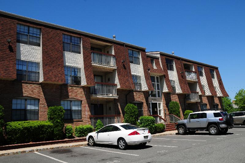 Hidden Village exterior photo showing a 3 story apartment building with balconies. A large parking lot supplies ample parking for tenants.