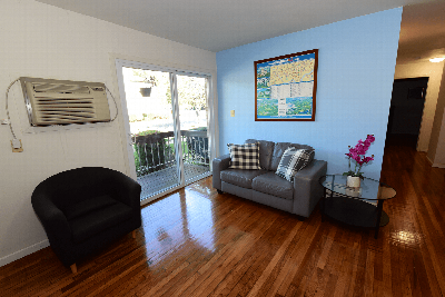 Florida Grove Arms image of the living room features a couch, with hardwood floors leading to sliding glass door to the balcony.